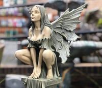 a statue of a woman sitting on top of a wooden post in a store aisle