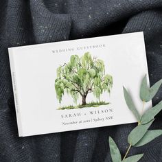 the wedding guest book is laying on top of a blanket with an olive branch in front of it