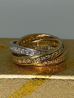 two gold rings with diamonds on top of a golden box next to a yellow ribbon