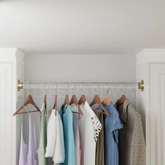 clothes hanging on hooks in a closet with white cabinets and doors behind them is a row of folded towels