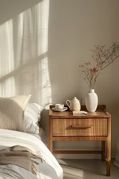 a wooden table with two cups on it next to a white vase and bedding