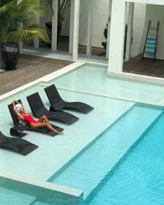 a woman laying on lounge chairs next to a swimming pool