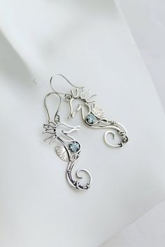 two silver seahorse earrings with blue topazte and white pearls, on a white background