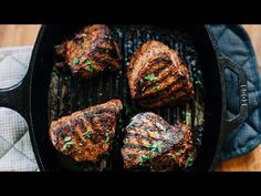 steaks cooking in a cast iron skillet on top of a wooden table next to a towel