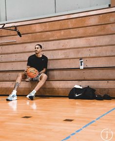 a man sitting on a bench with a basketball in his hand and another bag next to him