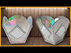 two silver vases sitting next to each other on top of a wooden floor covered in lots of cd's