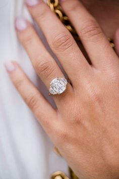 a woman's hand with a diamond ring on top of her finger and gold chains around it