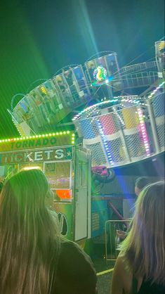 two women are standing in front of a carnival ride at night with lights on it