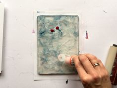 a person is painting on a piece of paper with acrylic paint and glue