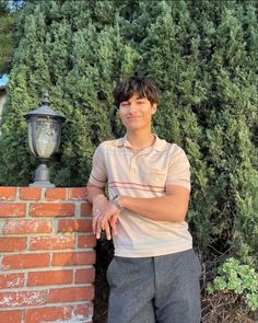 a young man leaning against a brick wall next to a lamp post and shrubbery