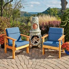 two wooden chairs sitting next to each other near a fire place in the middle of a garden