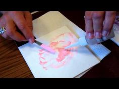 two hands are using a sharpie to draw a face on paper with pink ink