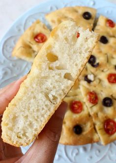 a person holding a piece of bread with olives and tomatoes on it