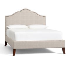 an upholstered bed with white sheets and pillows