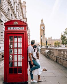 a man and woman standing next to a red phone booth