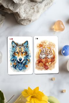 two cards with animals on them sitting next to some rocks and flowers in vases