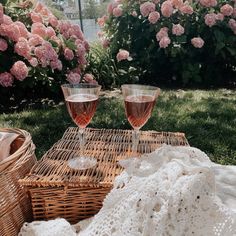 two wine glasses sitting on top of a wicker basket next to pink hydrangeas