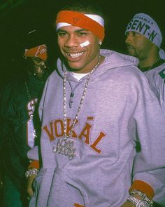 a man wearing a red and white head band smiles at the camera while standing next to other men