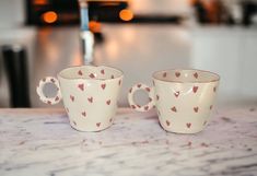 two coffee cups with hearts painted on them sitting on a counter top next to each other