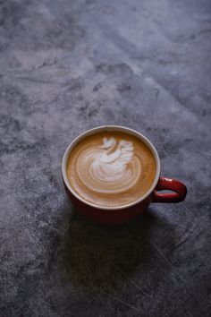 a cappuccino in a red cup sitting on top of a gray table