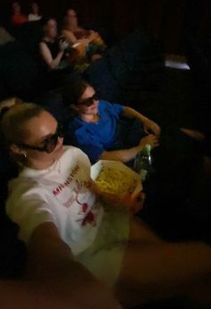 two people sitting in a movie theater, one holding a bottle and the other eating popcorn