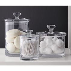 three glass containers with white cotton swabs in them on a countertop next to each other