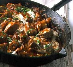 a skillet filled with meat and vegetables on top of a wooden table