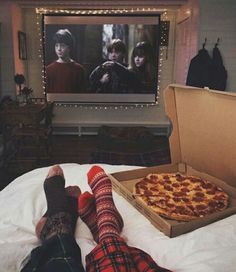 two people laying on a bed in front of a tv with a large pizza in it