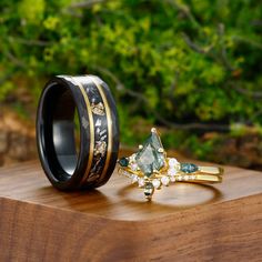 two wedding rings sitting on top of a wooden table next to each other with green and white stones