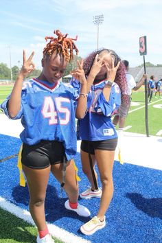 two young women standing on top of a football field holding their hands in the air