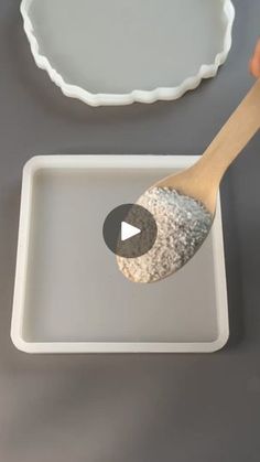 a person holding a wooden spoon in front of a white tray with an empty pan