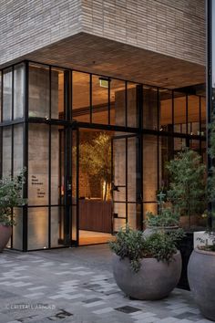 an entrance to a building with large planters on the sidewalk and potted trees in front