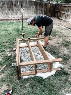 a man working on an unfinished bed frame in the yard with tools and materials around him