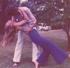 a man and woman are kissing in the grass with trees in the back ground behind them