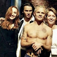 a group of people standing next to each other in front of a brick wall with tattoos on their chests