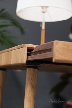 a close up of a wooden table with a lamp in the background and a plant behind it