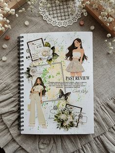 an open notebook with paper dolls and flowers on it next to a lace doily