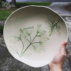 a hand holding a white bowl with green leaves painted on the side and words that read citrus basil