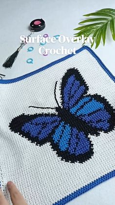 a crocheted blue butterfly on a white blanket next to a plant and scissors