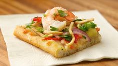 a piece of pizza with shrimp and veggies on it sitting on a napkin