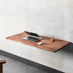 a laptop computer sitting on top of a wooden desk next to a wall mounted shelf