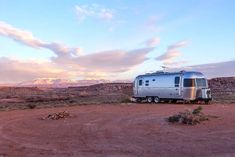 an rv is parked in the desert with mountains in the backgroud and clouds in the sky