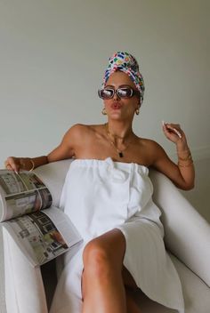 a woman sitting in a chair with her legs crossed and reading a newspaper while wearing sunglasses