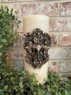 a white candle sitting on top of a table next to some plants and a brick wall