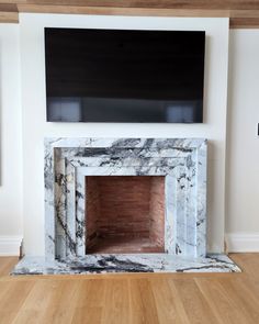 a fireplace with a tv above it in a room that has wood floors and white walls