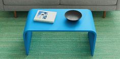 a blue coffee table with a book and bowl on it next to a gray couch