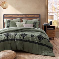 a bed with green comforter and pillows in a room next to a basket on the floor