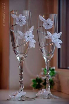 two wine glasses decorated with white flowers and beaded pearls are sitting on a table