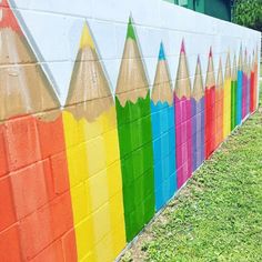 there are many colored pencils painted on the side of this brick wall and grass