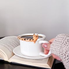 a person is holding a coffee cup with a cat on it and an open book